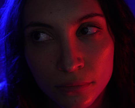 Extreme close-up of a woman's face lit by blue and red light, gazing sideways in horror film Goody Goody