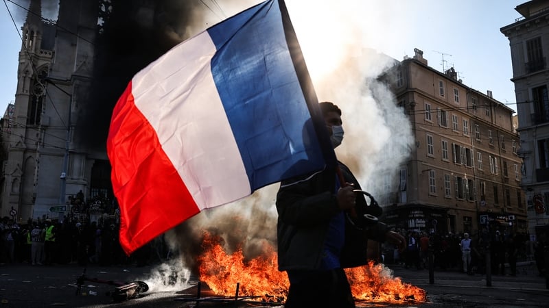 A protester waving a French national flag walks past a fire during clashes prior to the start of a demonstration to protest against the "high cost of living", in Marseille