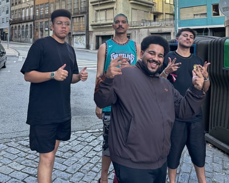 Four men from the band Weird Baile pose on a cobbled street, making peace signs and smiling
