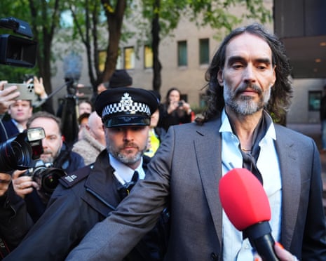 Russell Brand is escorted past reporters and photographers outside court