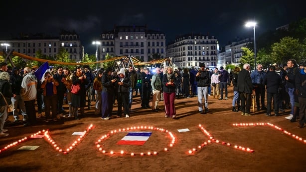 lit candles spell out Lyon as people gather around them